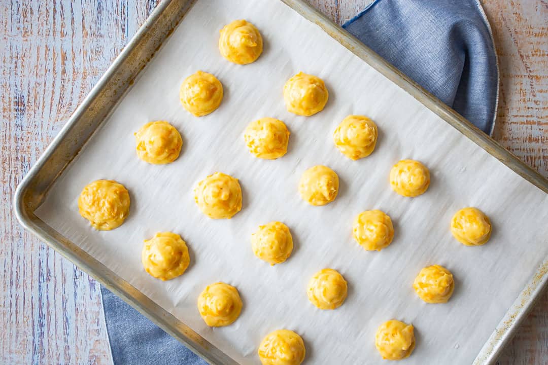 Unbaked cheese puffs piped on a baking sheet.