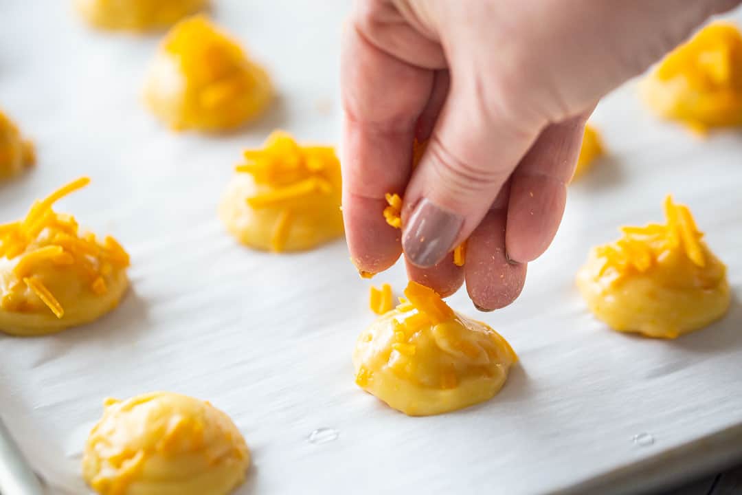 Sprinkling cheese on unbaked choux puffs.