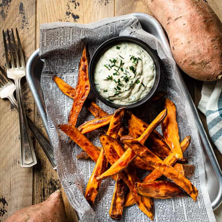 Sweet potato fries on a metal sheet pan with a bowl of creamy dipping sauce.