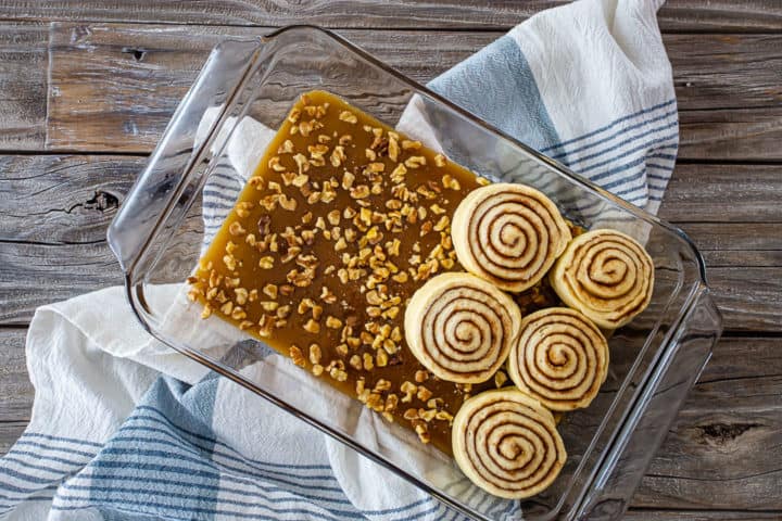 Placing unbaked sticky buns in a glass baking dish, on top of the sticky bun topping.