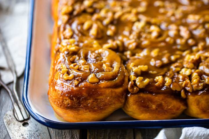 Close-up image of homemade sticky buns on a white tray with a vintage cake server.