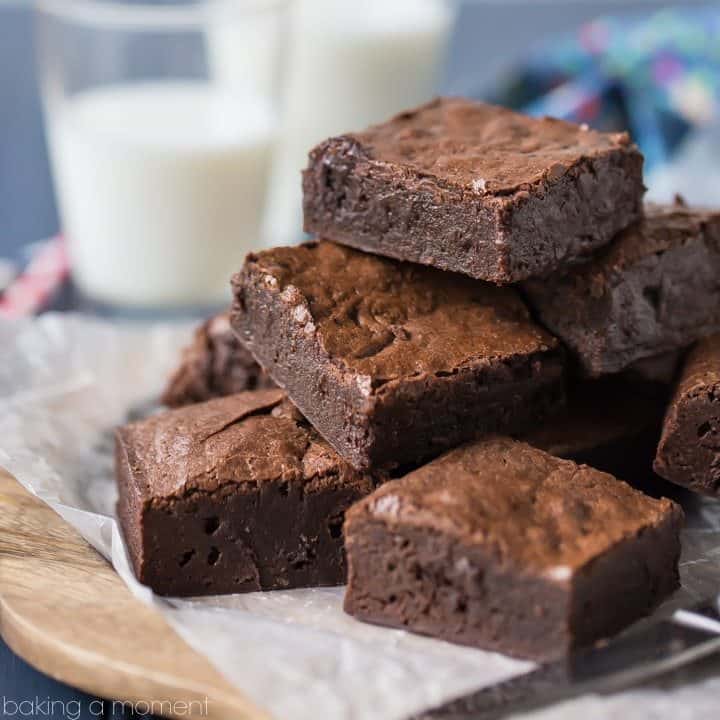 Brownies on a wood plate with a glasses of milk in the background.