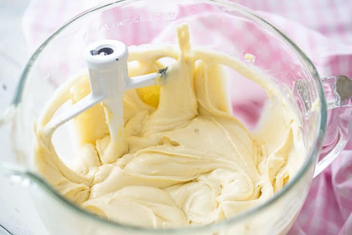 Yellow cake batter in a large glass mixing bowl with the paddle attachment.