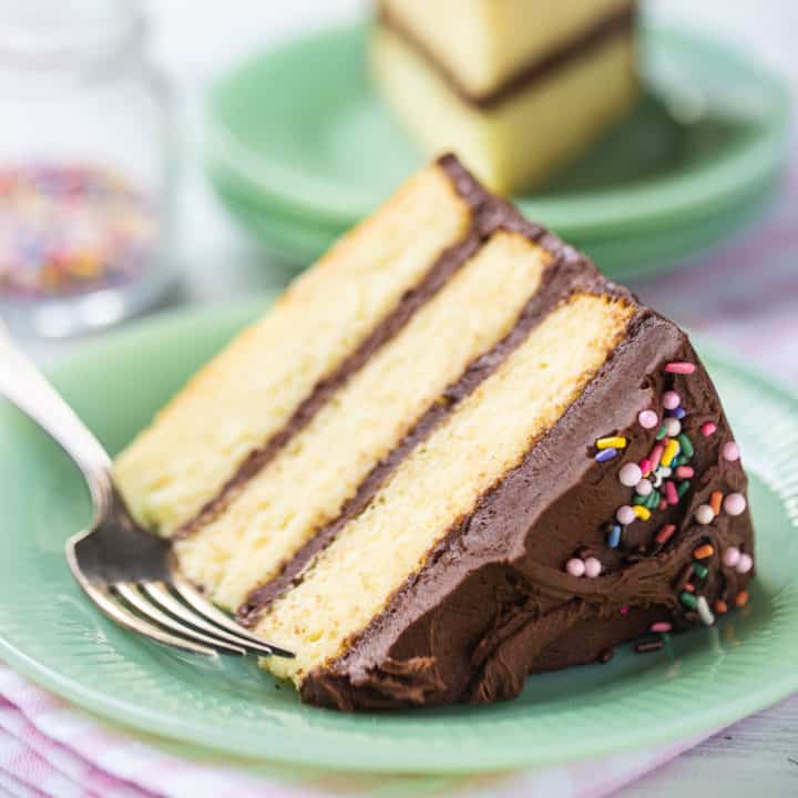Yellow cake recipe, baked in 3 layers, frosted with chocolate buttercream, and served on a pale green plate.