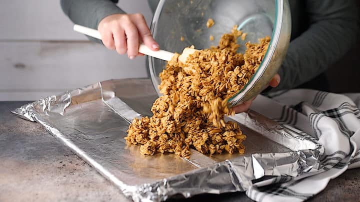 Tipping unbaked granola from the bowl onto a foil-lined baking sheet.