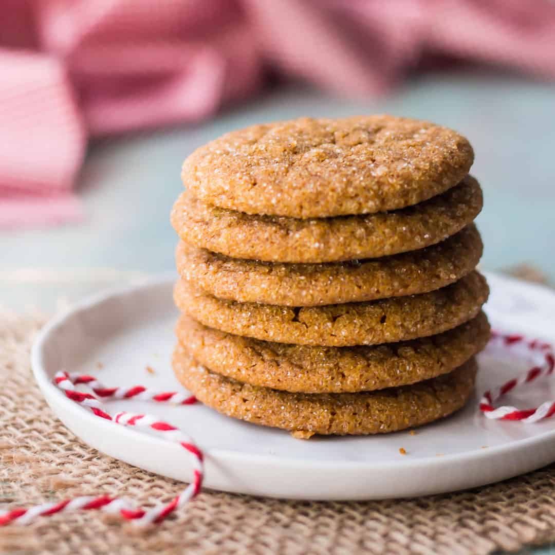 A stack of soft ginger cookies on a small white plate with red and white baker's twine.