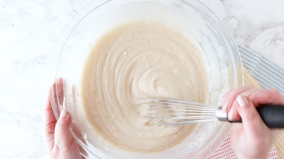Whisking coconut cake batter in a large glass mixing bowl.