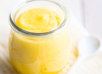 Small jar of homemade lemon curd on a yellow checked cloth.