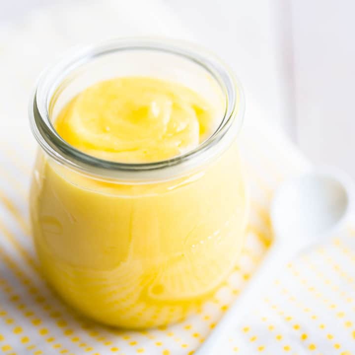 Small jar of homemade lemon curd on a yellow checked cloth.
