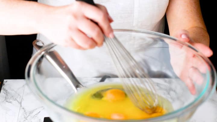 Whisking eggs, sugar, & lemon juice together in a large bowl over a pot of simmering water.