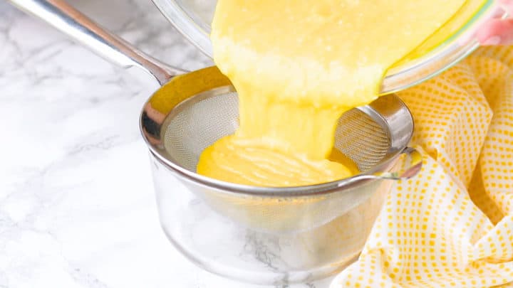 Straining lemon curd into a heat safe bowl.