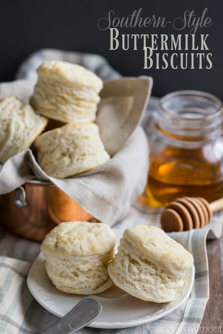 Two buttermilk biscuits on an antique china plate, with a basket of biscuits and a jar of honey in the background.