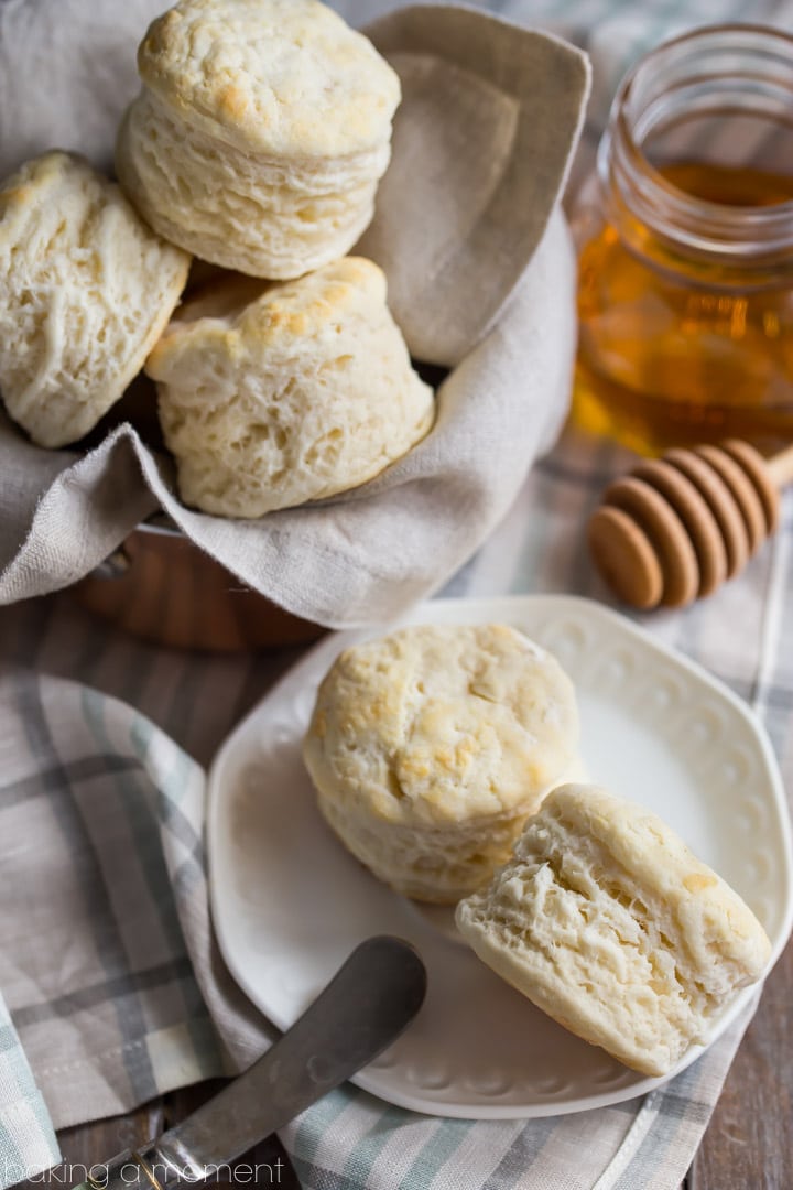Close-up image of homemade buttermilk biscuits on a checkered cloth, with a jar of honey in the background.
