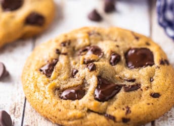Close up image of a chocolate chip cookie on a distressed white table, surrounded by chocolate chips.