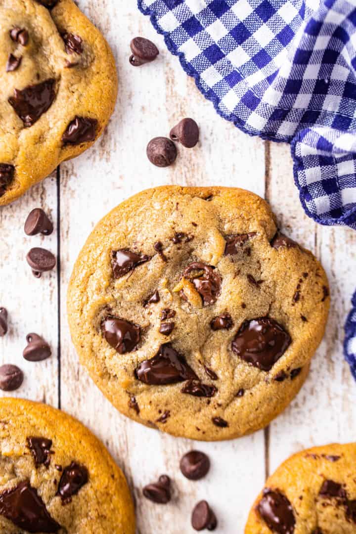 Overhead image of the best chocolate chip cookie recipe, baked and scattered on a board with a blue checked napkin.