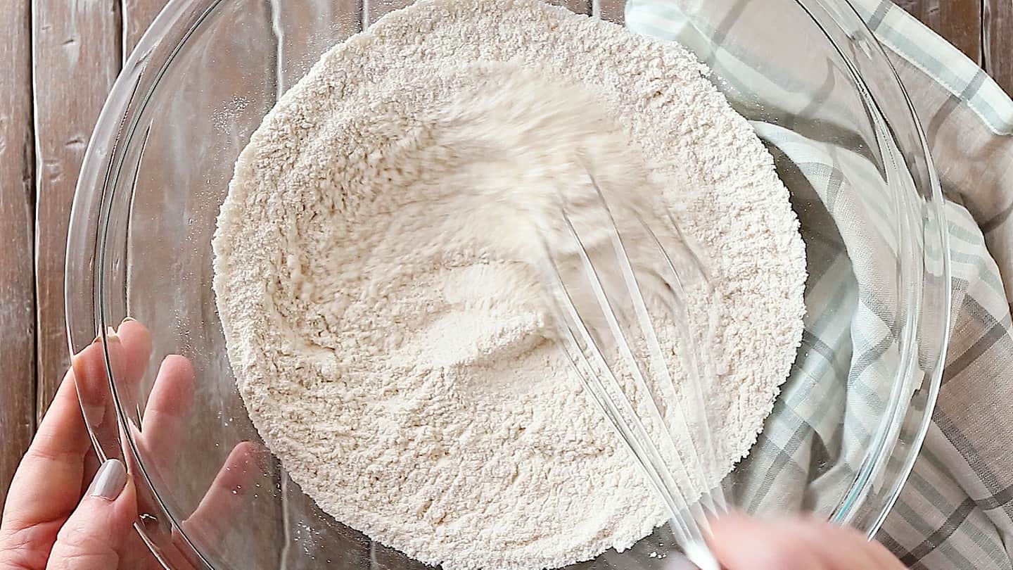 Flour, baking powder, and salt being stirred together in a large glass mixing bowl.