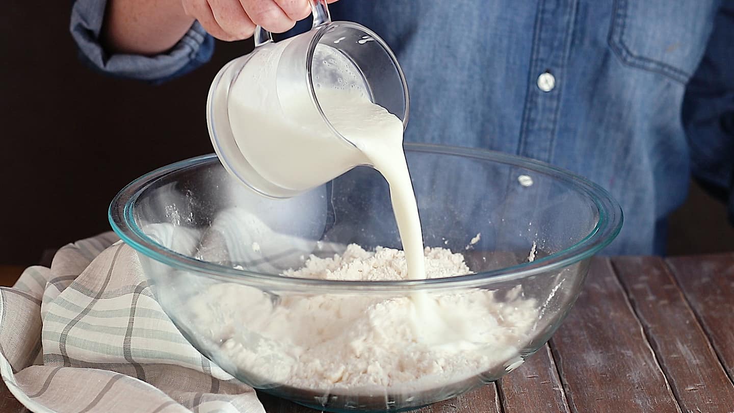 Pouring buttermilk into a mixing bowl to make biscuits.