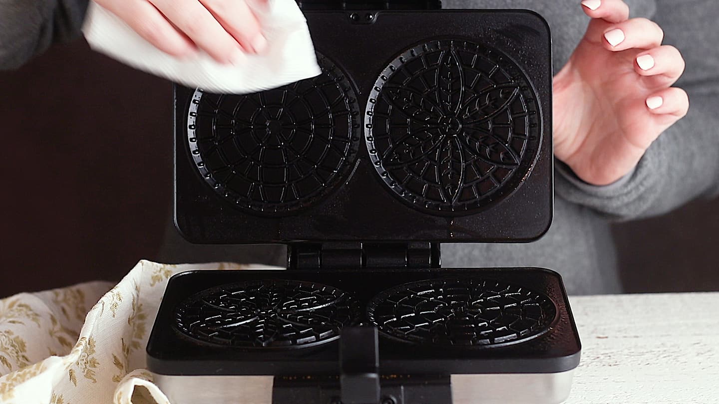 Lightly greasing a pizzelle maker.