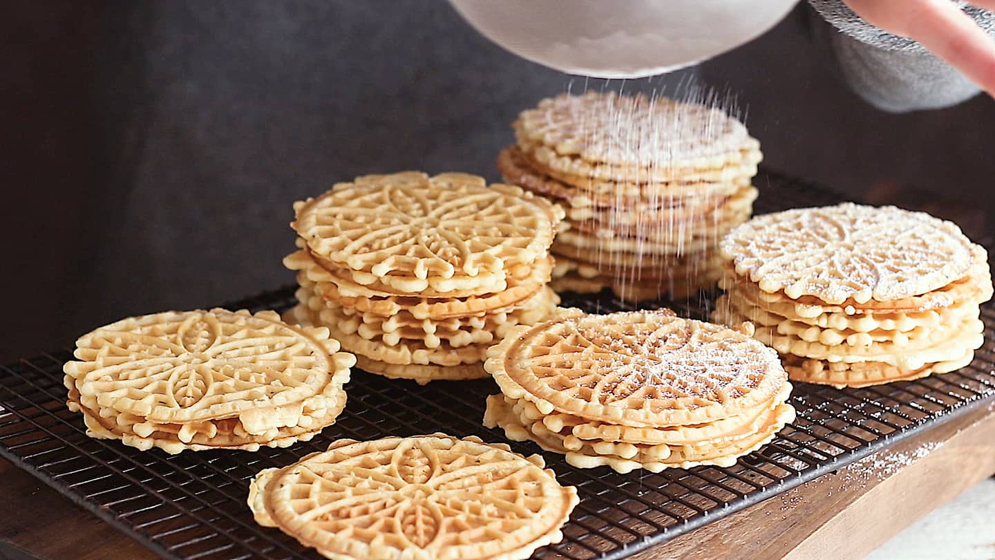 Dusting pizzelle cookies with powdered sugar.