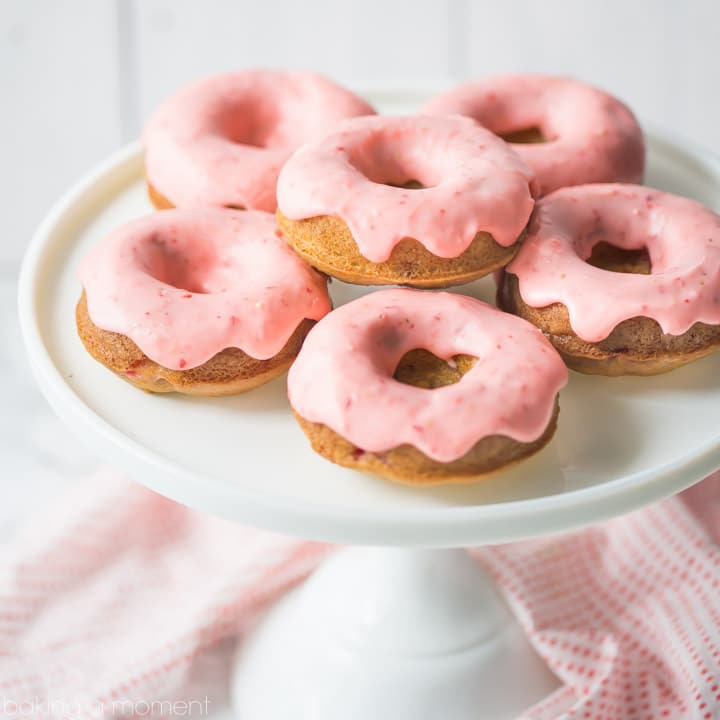 Baked strawberry donuts with pink strawberry icing, on a white cake stand. 