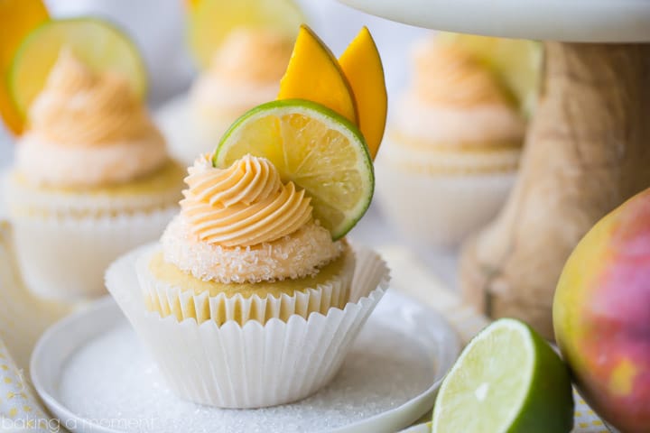 Mango Margarita Cupcakes: a yellow mango and lime cupcake with a salted rim and a swirl of mango margarita buttercream on top, garnished with lime and sliced mango