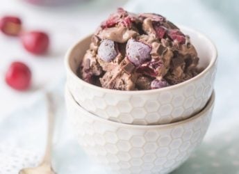 A bowl of chocolate ice cream, studded with dark sweet cherries and chocolate chunks.