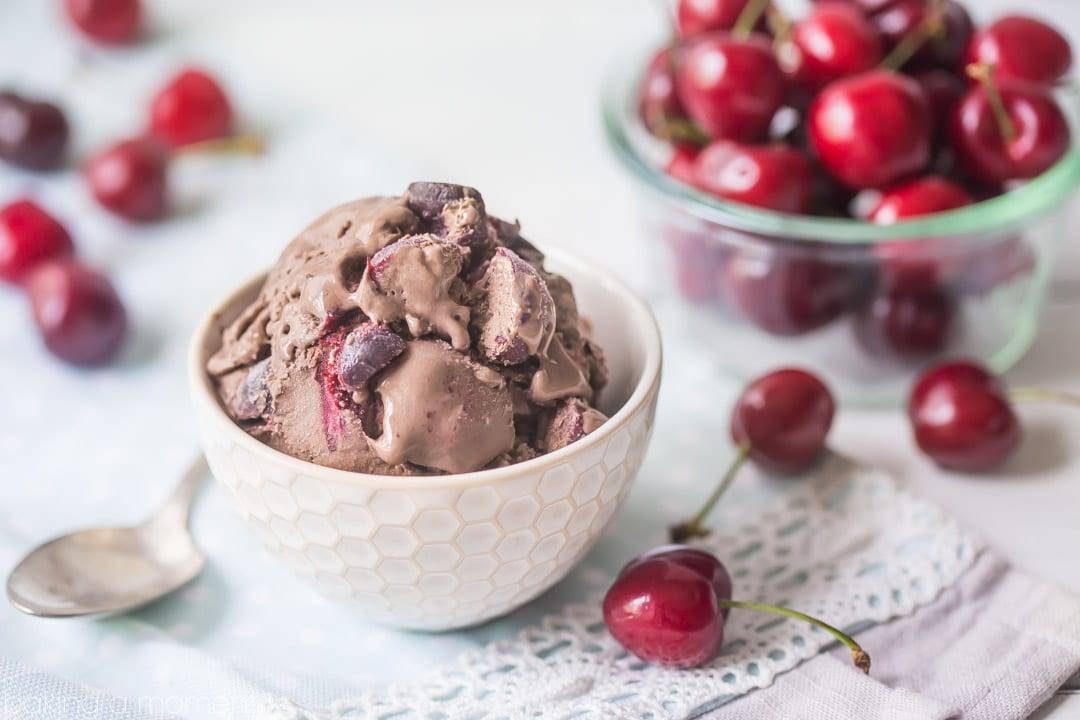 A bowl of chocolate ice cream, studded with dark sweet cherries and chocolate chunks. 