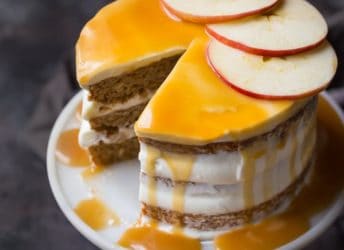 Triple-layer apple honey cake on a cake stand, with cream cheese frosting and honey caramel drizzle, garnished with fresh apple slices.