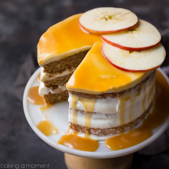 Triple-layer apple honey cake on a cake stand, with cream cheese frosting and honey caramel drizzle, garnished with fresh apple slices. 