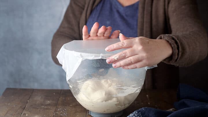 Covering bread dough with plastic wrap.