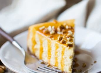 Slice of caramel pecan cheesecake on a plate, drizzled with caramel sauce and sprinkled with chopped pecans.