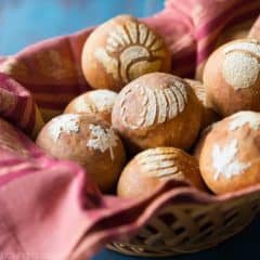 Basket lined with a red cloth, filled with bread rolls stenciled with fall/Thanksgiving themed images, on an aqua tabletop.