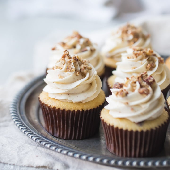 Five butter pecan cupcakes topped with swirls of brown butter frosting and sprinkled with pecans, on an antique silver platter.
