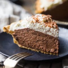 A tall slice of chocolate pie with whipped cream on a dark blue plate.