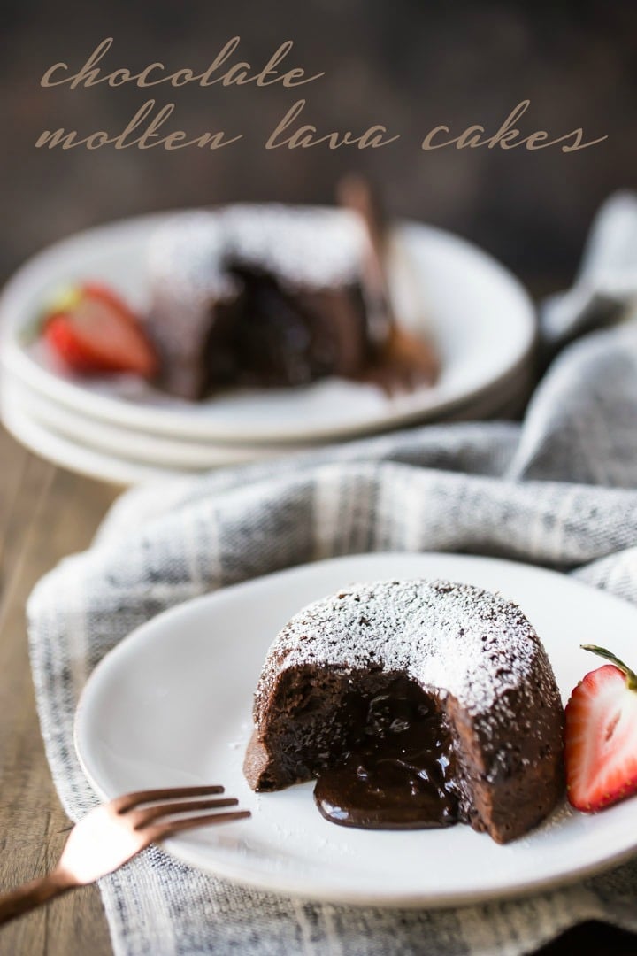Chocolate Molten Lava Cake on a white plate, with liquid chocolate spilling from the center. Garnished with a strawberry, and a linen cloth beneath the plate and a copper fork on the side.