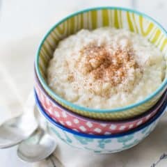 Three colorful bowls stacked on a linen napkin, filled with a creamy rice pudding and sprinkled with cinnamon.