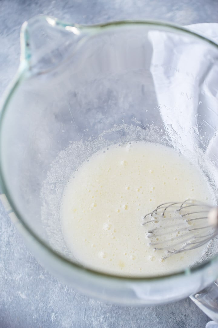 Cooked egg whites and sugar in a glass mixing bowl with a whisk.