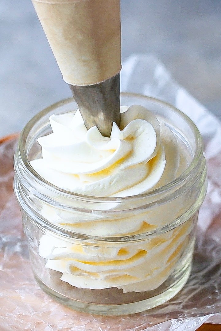 Swiss meringue buttercream being piped into a small glass jar.