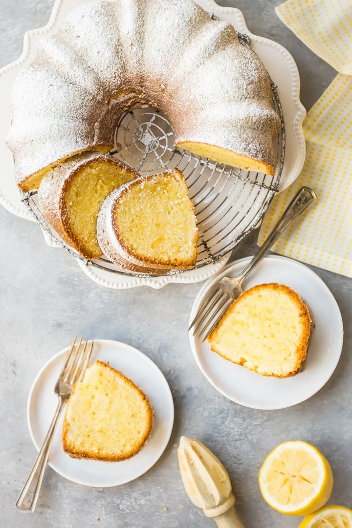 Overhead view of a sliced lemon pound bundt cake on a cooling rack over a yellow napkin, with cake slices on white plates with silver forks nearby.