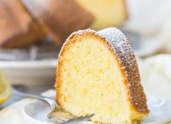 A tall slice of buttery lemon pound cake on a white plate over a yellow napkin, with a silver fork alongside.