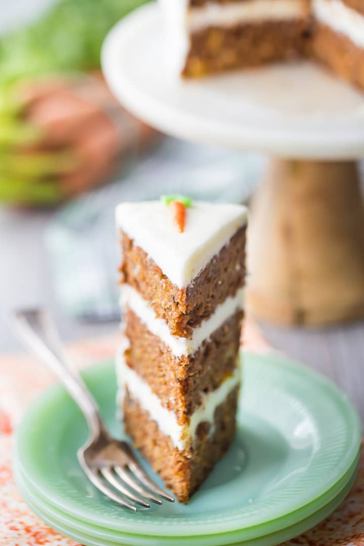 Tall slice of triple-layer carrot cake with cream cheese frosting, on a green plate with an orange napkin below.