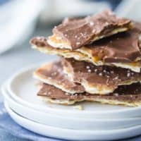 Square image of a stack of matzo toffee on a small white plate, with a blue napkin underneath.