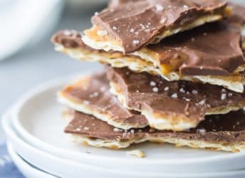 Square image of a stack of matzo toffee on a small white plate, with a blue napkin underneath.