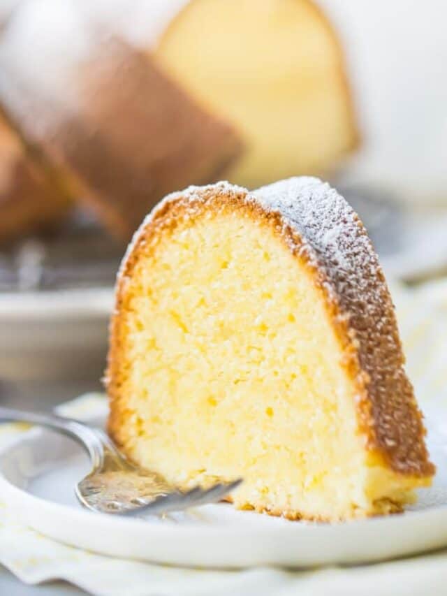 A tall slice of buttery lemon pound cake on a white plate over a yellow napkin, with a silver fork alongside.