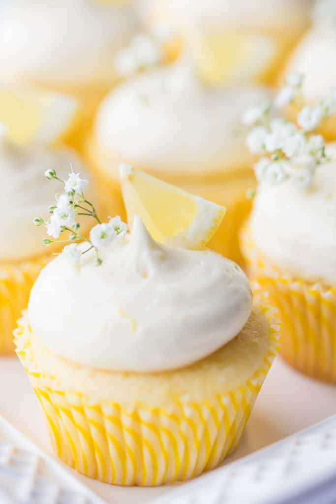 Vertical image of lemon cupcakes with lemon curd filling and lemon cream cheese frosting, garnished with lemon wedges and baby's breath.