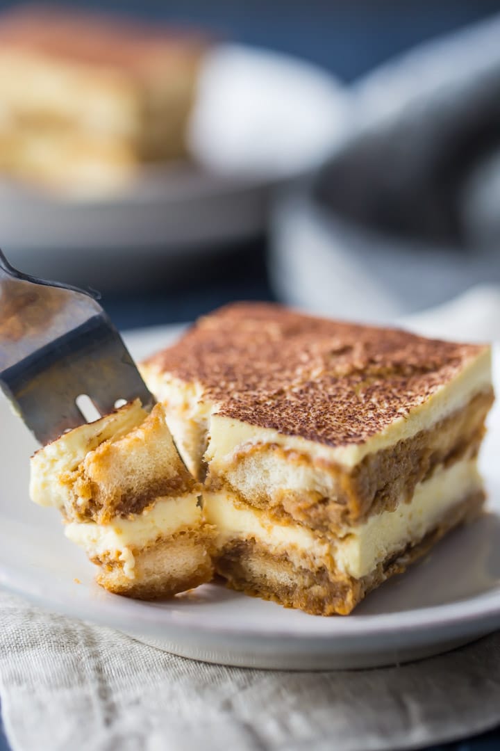 Vertical image of a slice of tiramisu with a fork taking out a bite.