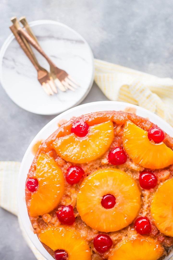 Vertical overhead image of a pineapple upside down cake with marbelized plates, copper forks, and a yellow napkin.