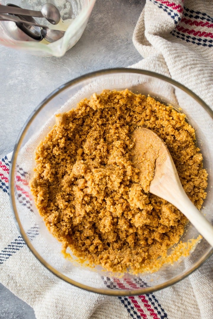 Graham cracker crust stirred together in a glass bowl with a wooden spoon.