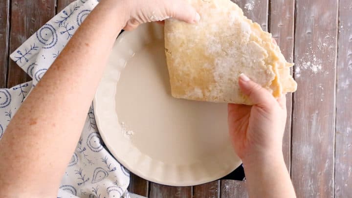 Transferring folded pie crust dough into a pie dish.