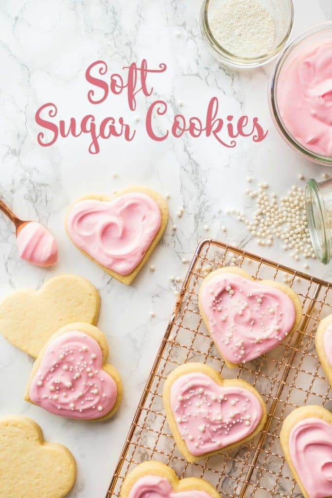 Vertical image of soft rolled sugar cookies on a copper cooling rack, with pink sour cream frosting.